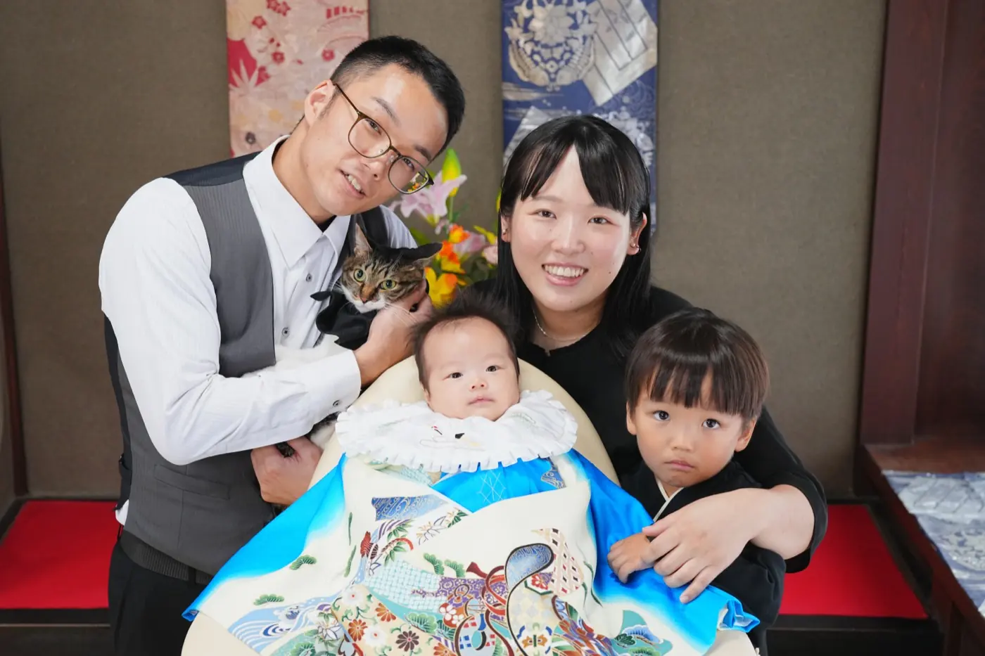 青い祝い着の赤ちゃんを囲む、パパ・ママ・お兄ちゃんとねこの家族写真