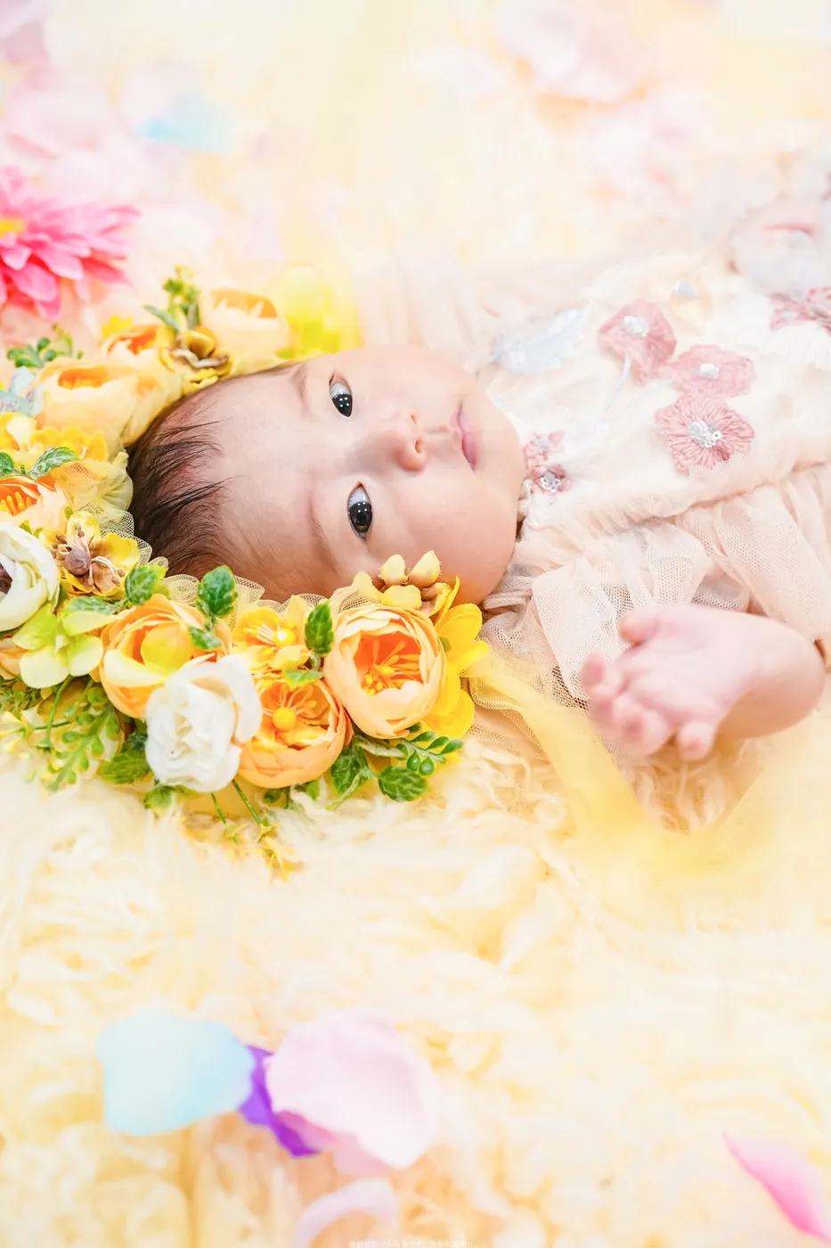 黄色いお花の冠をつけて、ふわふわの上に寝ころぶ赤ちゃん