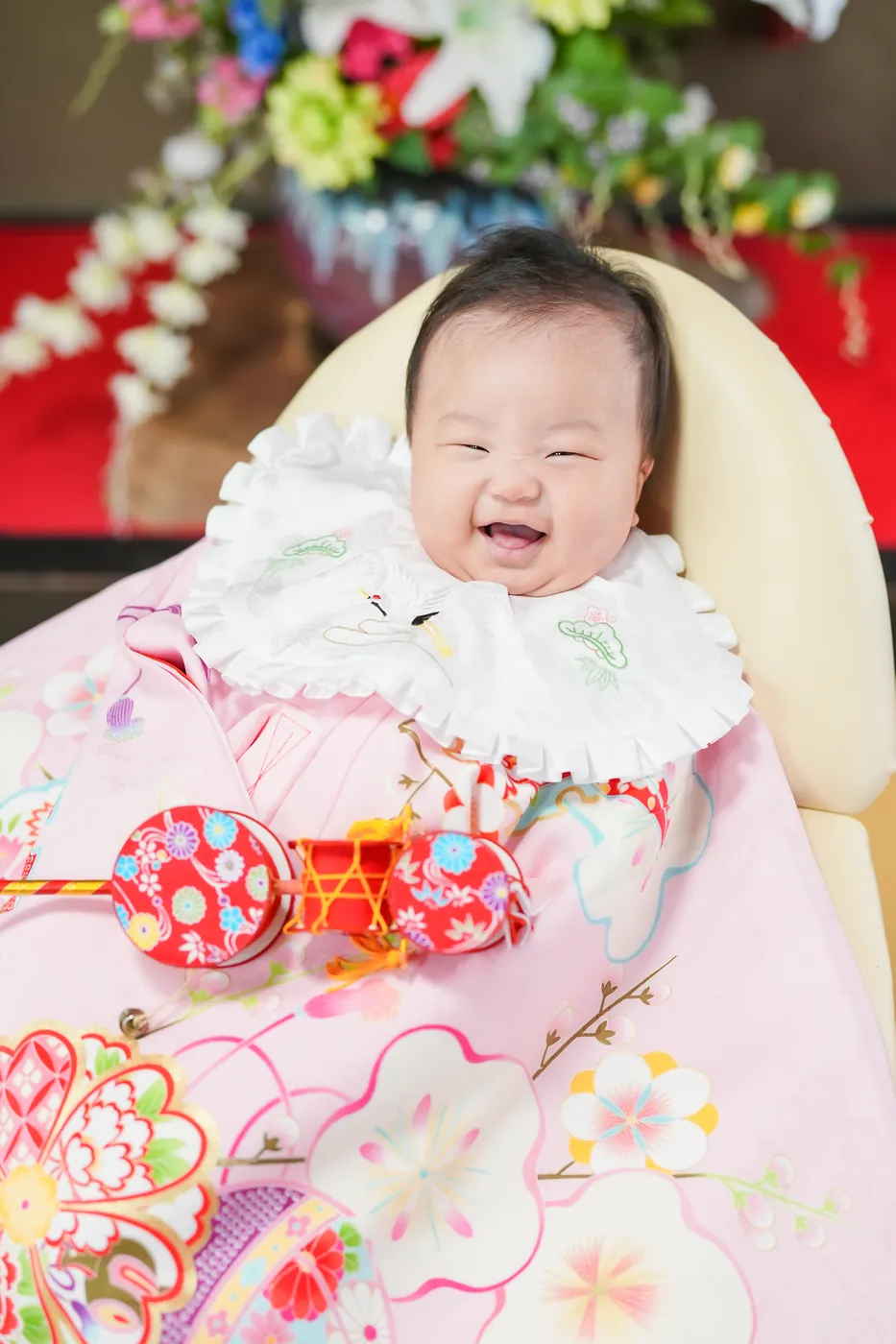 ピンクの祝い着をかけて、にっこり笑う生後1か月ごろの赤ちゃん