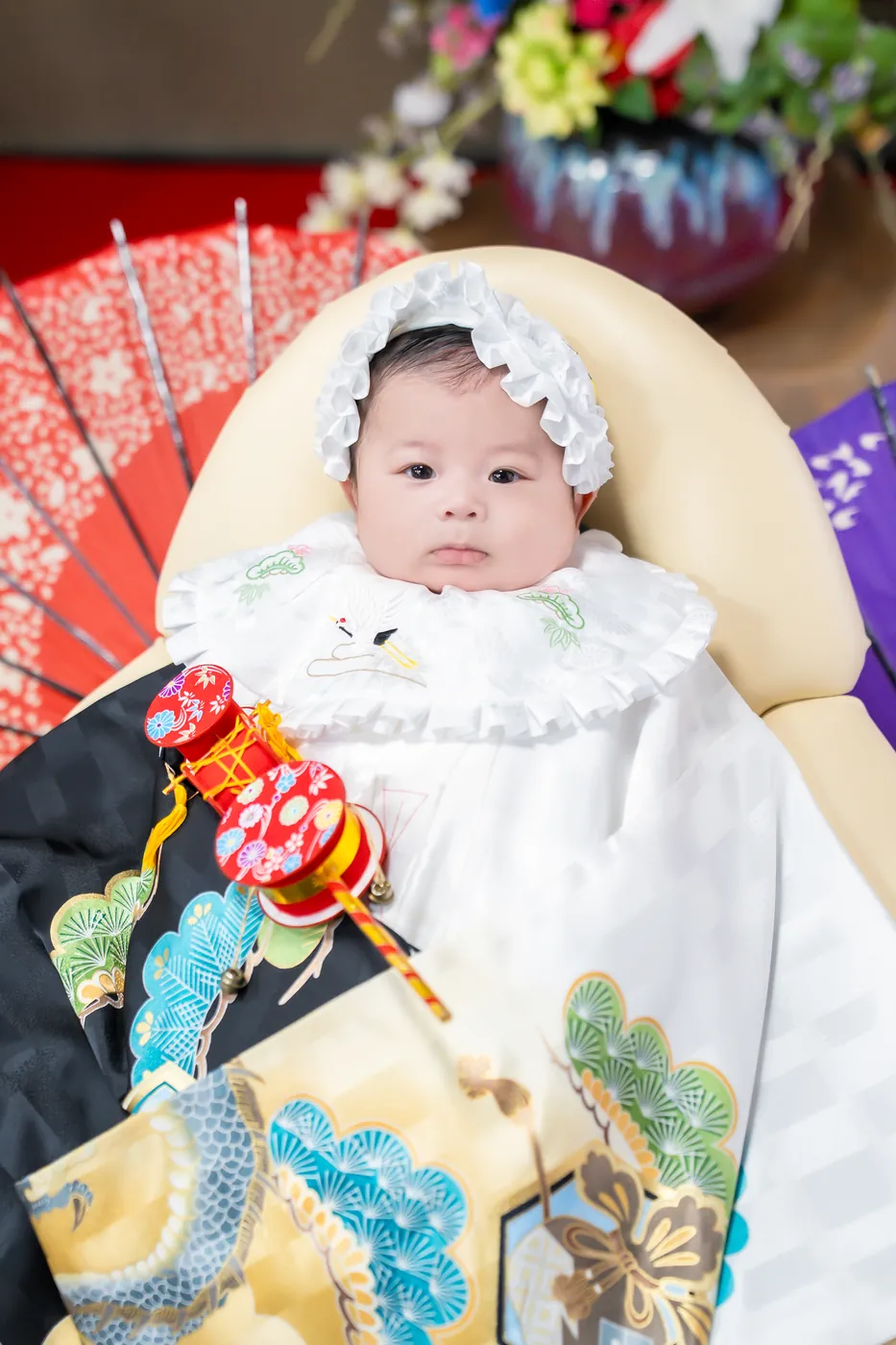 和傘の前で、松と鷹の祝い着をかけた男の子の赤ちゃん