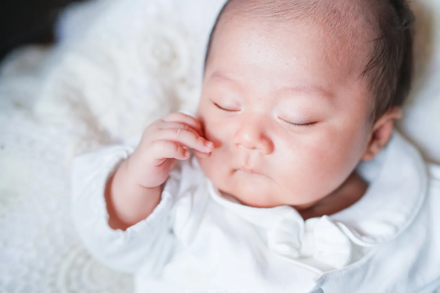 白い産着でほっぺに手をあててねむる赤ちゃん