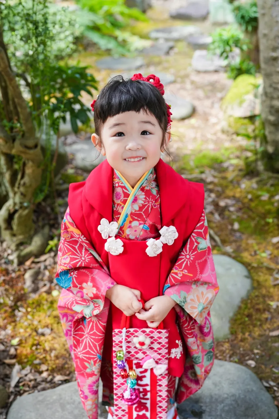 庭で手を合わせる赤い被布の3歳女の子