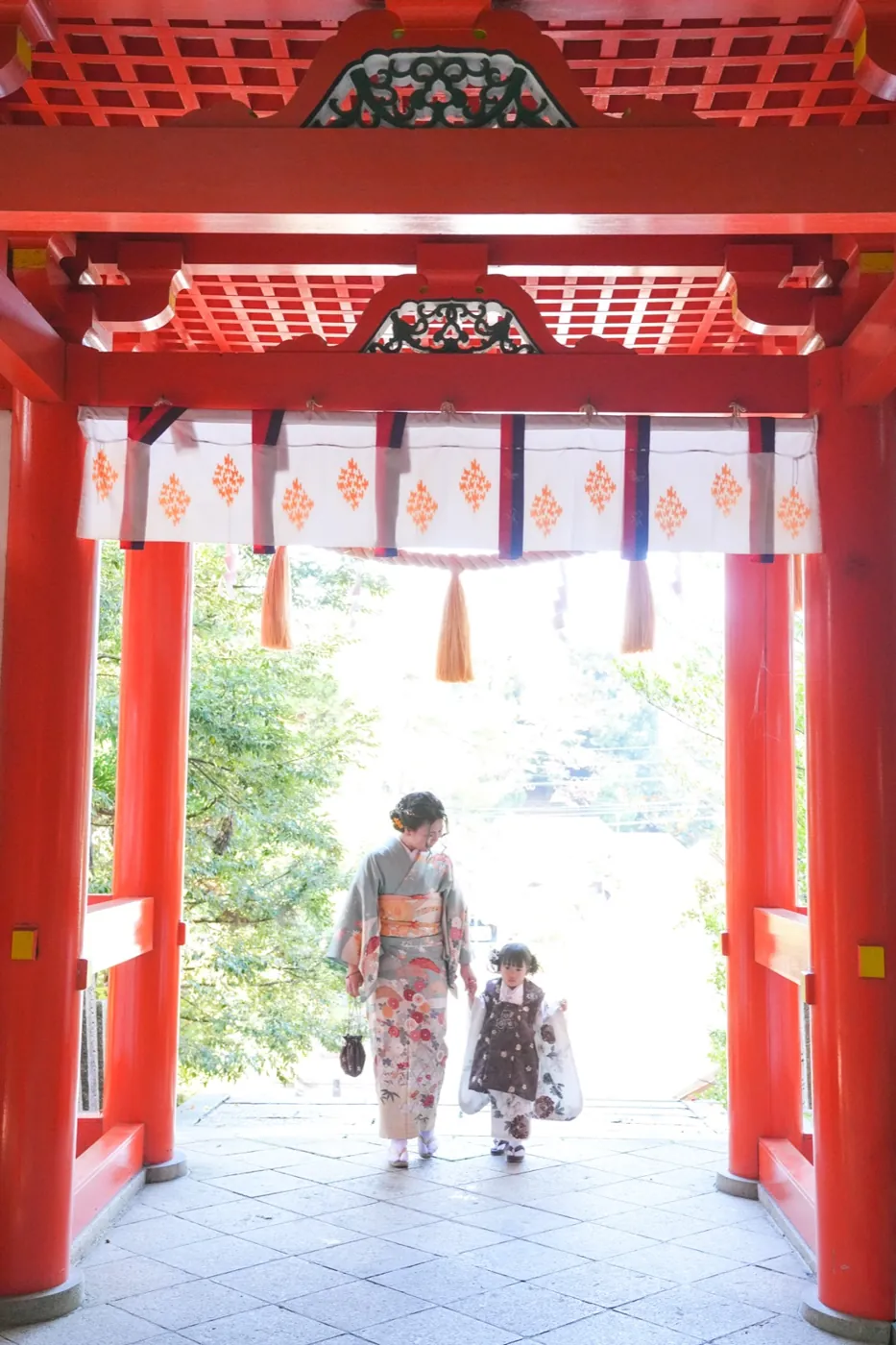 朱色の鳥居の下を着物姿で歩く母と子